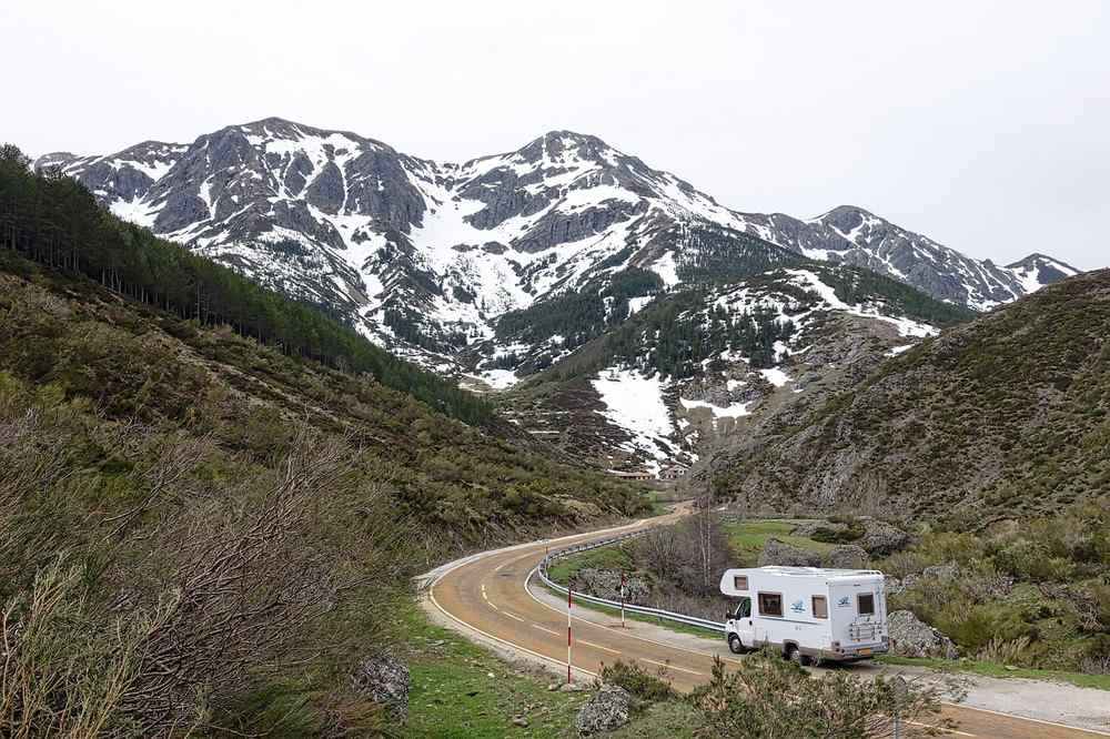 Une caravane suit une route courbée au pied des montagnes enneigées
