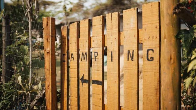 Barrière en bois avec inscription CAMPING et flèche, entourée de végétation