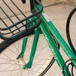 Vélo vert équipé d'un panier métallique, stationnné sur route