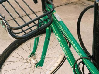 Vélo vert équipé d'un panier métallique, stationnné sur route