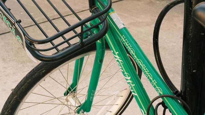 Vélo vert équipé d'un panier métallique, stationnné sur route