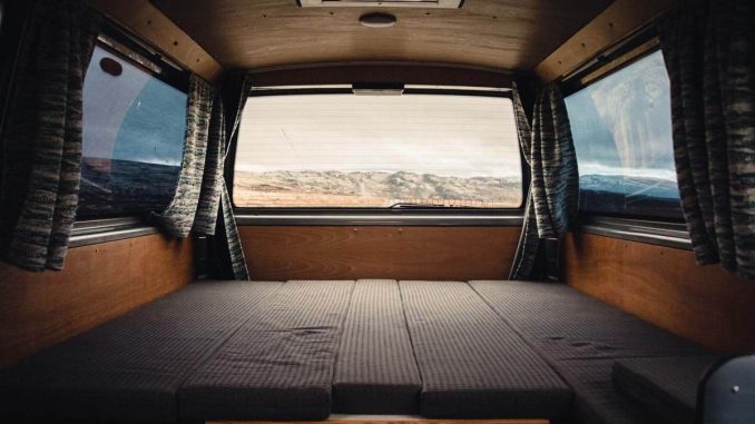 Intérieur d'un véhicule camper avec lit pliant, rideaux et vue extérieure